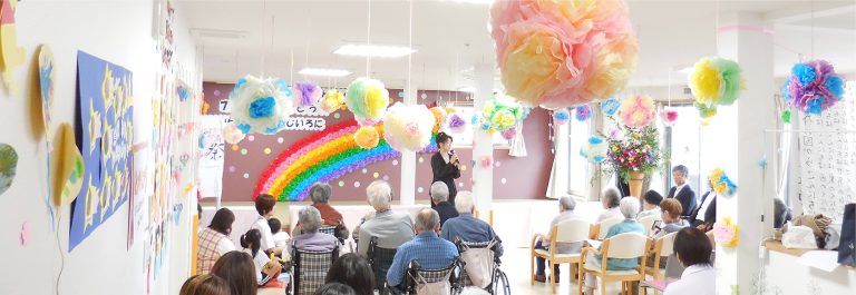 カラフルな装飾で彩られた室内でレクリエーション行事が開催され、入居者が参加している様子